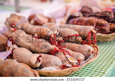 Closeup picture of fresh meat sausages with red strings on tabletop. Spicy delicatessen on blurred market indoor background.