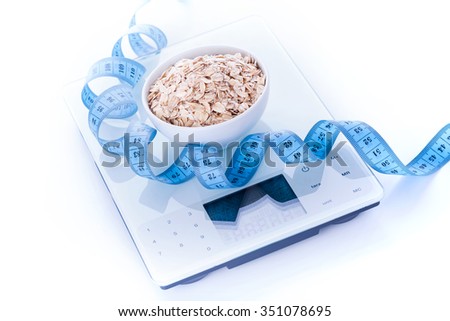 Portion of oatmeal in bowl on electronic kitchen scales with measure tape. Weight loss and diet concept.