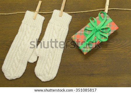 Two white mittens and red-and-green box hanging on a rope