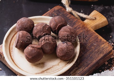 Rustic wooden boards with truffle candies on ceramic plate glass sugar bowl, served with sugar sticks and chocolate chips over dark background