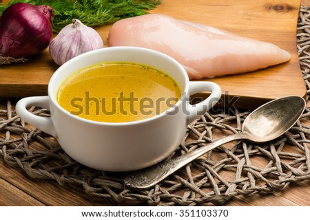 Chicken bouillon in the white bowl on the rustic wooden background.