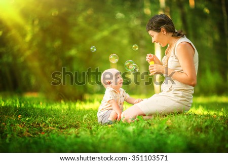 Happy mother and baby blowing bubbles in the summer park.