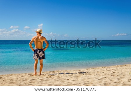 A handsome man in swimming trunks standing on exotic caribbean beach and looking out to sea, Cuba, the Caribbean, Central America Royalty-Free Stock Photo #351170975