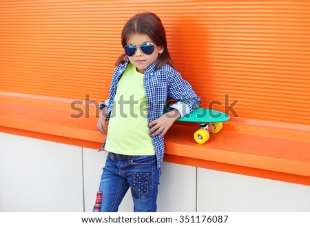 Fashion kid on skateboard wearing a sunglasses and checkered shirt over orange background