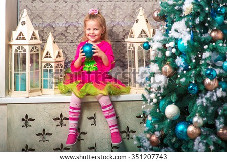 little pretty curly blonde smiling girl sitting on the windowsill nearly Christmas tree with Christmas decorations and presents