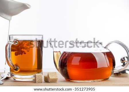 Spilled milk for cup of tea. Transparent cup and teapot on a white background