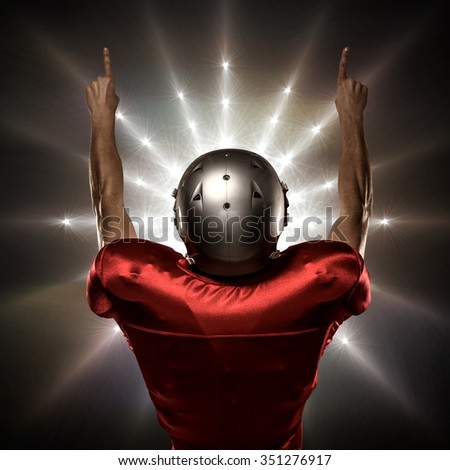 Rear view of American football player with arms raised against spotlight