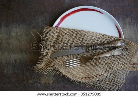 Plate and silverware on the old wooden table with burlap and napkin