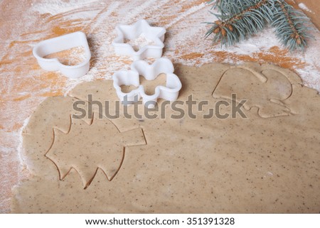 Dough for gingerbread cookie and cookie cutters in different shapes on light wooden cutting board like background.