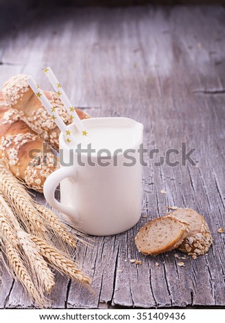 Jug with milk for breakfast and fresh homemade bread baguettes with ears on a simple wooden light background. The concept of healthy natural foods. selective Focus