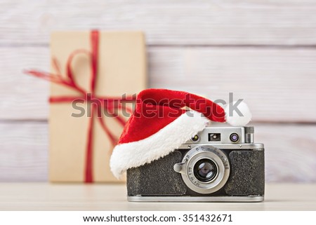 Old camera in santa hat over defocused gift box