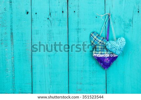 Purple and turquoise fabric hearts hanging on antique rustic teal blue wooden background