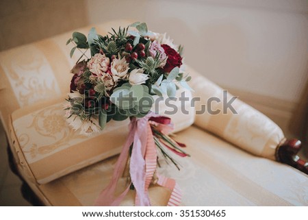 bouquet of flowers and greenery with a pink ribbon is on a vintage chair