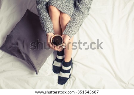 Color picture of a beautiful young woman drinking coffee at home in her bed wearing a cozy sweater