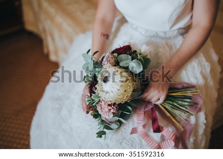 Bride sitting in a chair and holding a bouquet of pink flowers, white flowers and greenery with a pink ribbon