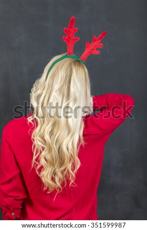 Pretty blond woman in a red reindeer Hat with a merry smile looking over her shoulder to blank copyspace on black for your Christmas greeting