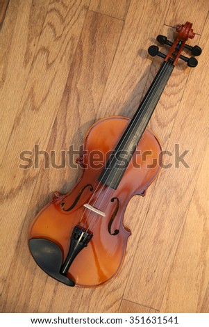 A 3/4 size Violin lays on a hard wood background with beautiful light and shadows for a unique view. Violins are part of the music world, some are worth millions of dollars.