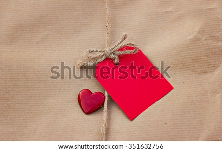 Gift in kraft paper with red card and heart on a wooden table. For Valentine's day