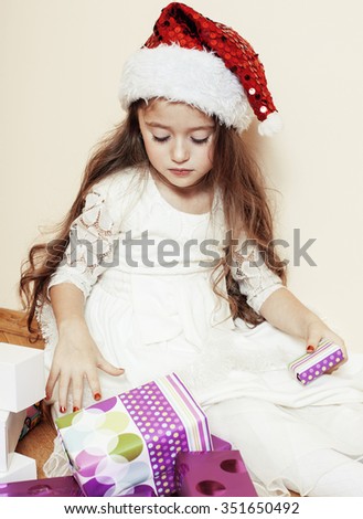 little cute girl in santas red hat waiting for Christmas gifts. smiling adorable kid. White new dress home interior. holding gift
