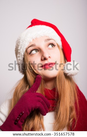 Christmas girl has a great idea for a gift on a gray background. Santa hat isolated portrait of a woman.