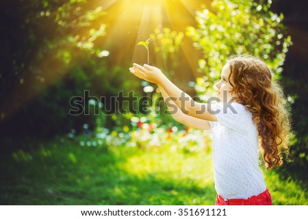 Little girl holding young green plant in sunlight. Ecology concept. Background toning to instagram filter.