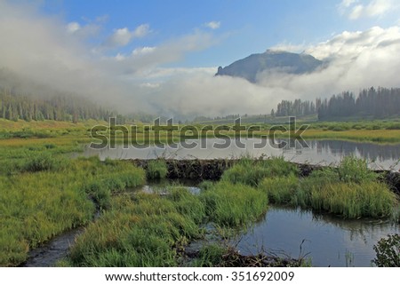 Beaver dam on Granite Creek Wyoming. Picture taken in early morning as clouds and low fog begin to reveal the calm water and mountain scenery.
