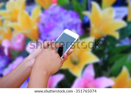 hand hold and touch screen smart phone, on abstract Blurred image flower bouquet background