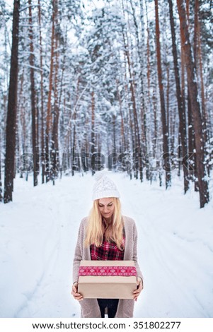 blonde girl holding a Christmas gift in winter forest
