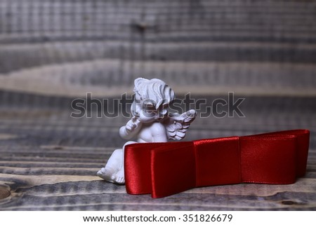 Closeup view of one beautiful cupid angel decorative figurine near red valentine silk ribbon bow with no people on wooden background copy space, horizontal picture