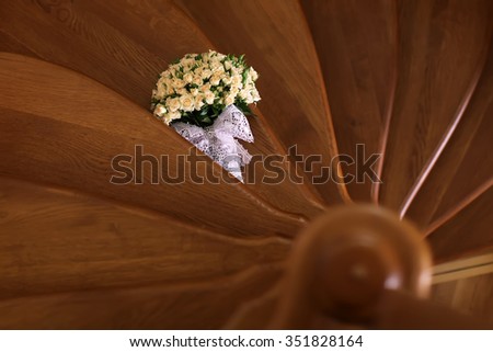 Photo of elegant bouquet of many beautiful fresh small pastel shade color tea roses flowers blossom buds green leaves with white bow on stair on timber spiral stairwell background, horizontal picture