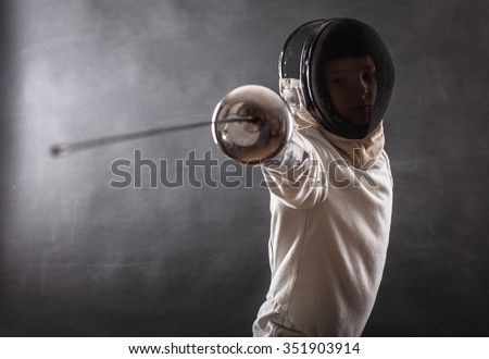 Boy wearing white fencing costume and black fencing mask standing with the sword practicing in fencing. Royalty-Free Stock Photo #351903914