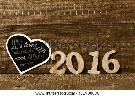 wooden numbers forming the number 2016 and a heart-shaped chalkboard with some wishes for the new year, such as peace, love and happiness, on a rustic wooden surface