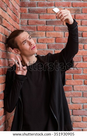 Portrait of a young man making selfie photo on smartphone oer brick wall background