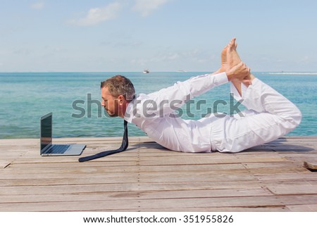 businessman doing yoga on a wooden bridge with a laptop