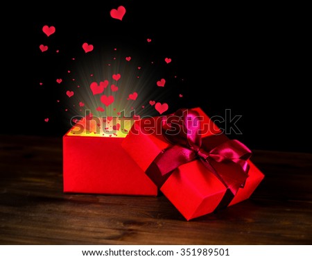 greeting opened box with bow and miracle light on wooden background is isolated on black, closeup