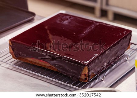 Square chocolate mousse cake with currant glaze at professional confectionery kitchen. Shallow focus