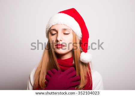 Christmas girl prays topic of religion. Santa hat isolated portrait of a woman on a gray background.