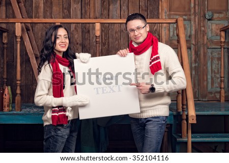 Picture of young family couple in a winter clothes holding white blank board. Beautiful pair dressed in winter Christmas clothes, hat, red scarf, and white sweater. 