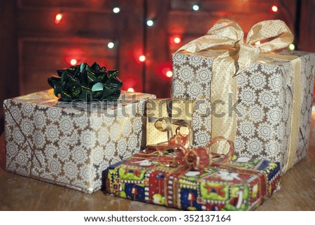 Several packaged Christmas or New Year gift boxes with bows and ribbons. The garland of blurry lights in the wooden background. The shabby table.