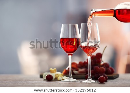 Pouring pink wine from bottle into the wineglass on blurred background Royalty-Free Stock Photo #352196012