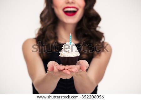 Cheerful beautiful curly young woman in retro style giving birthday cupcake with candle