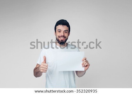 
The bearded student in a white T-shirt holding a blank sheet of paper. 
isolated on a light background .