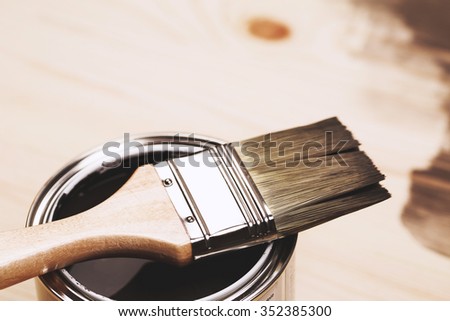 Paintbrush and a newly opened can of grey paint on wooden surface