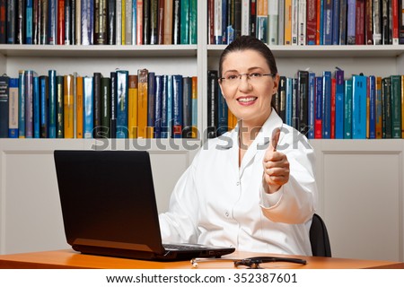 Smiling doctor with computer and a lot of books showing thumbs up, best, top online medical advice.