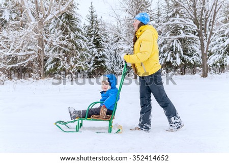 Mother walks with the son in the winter. She carries it on a sled through the snow