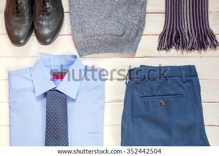collection of business modern men's clothing: black shoes, blue shirt, tie, blue pants, pullover, scarf for business travel on a white wooden background.  Top view. Business concept.