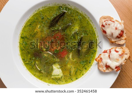 Serving of spicy fish soup Thai style in white plate, on top of brown wooden table