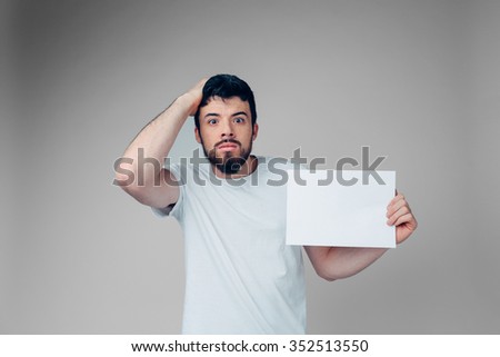 The bearded student in a white T-shirt holding a blank sheet of paper. 
isolated on a light background
 .