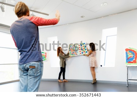 Young artists in gallery hanging together painting on walls