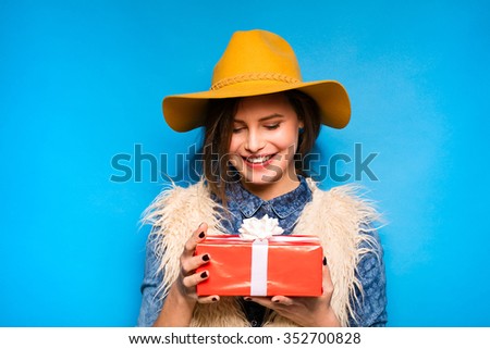 clouseup of young modern woman holding a red gift in hands, on blue background